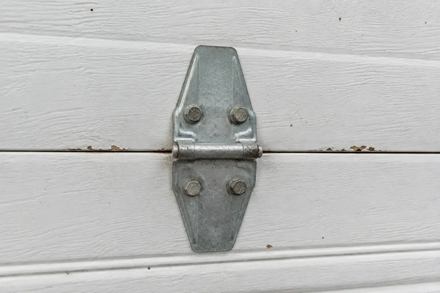 Metal center hinge across a seam in a white sectional garage door. — Garage Door Hinge Replacement, Brampton