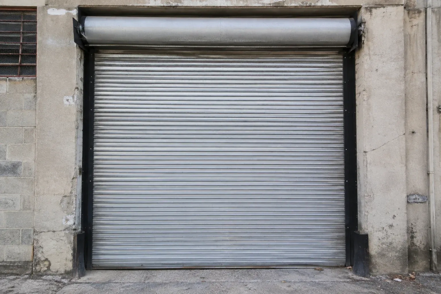 Closed metal rolling shutter in a weathered warehouse opening. — Commercial Rolling Door Repair, Brampton