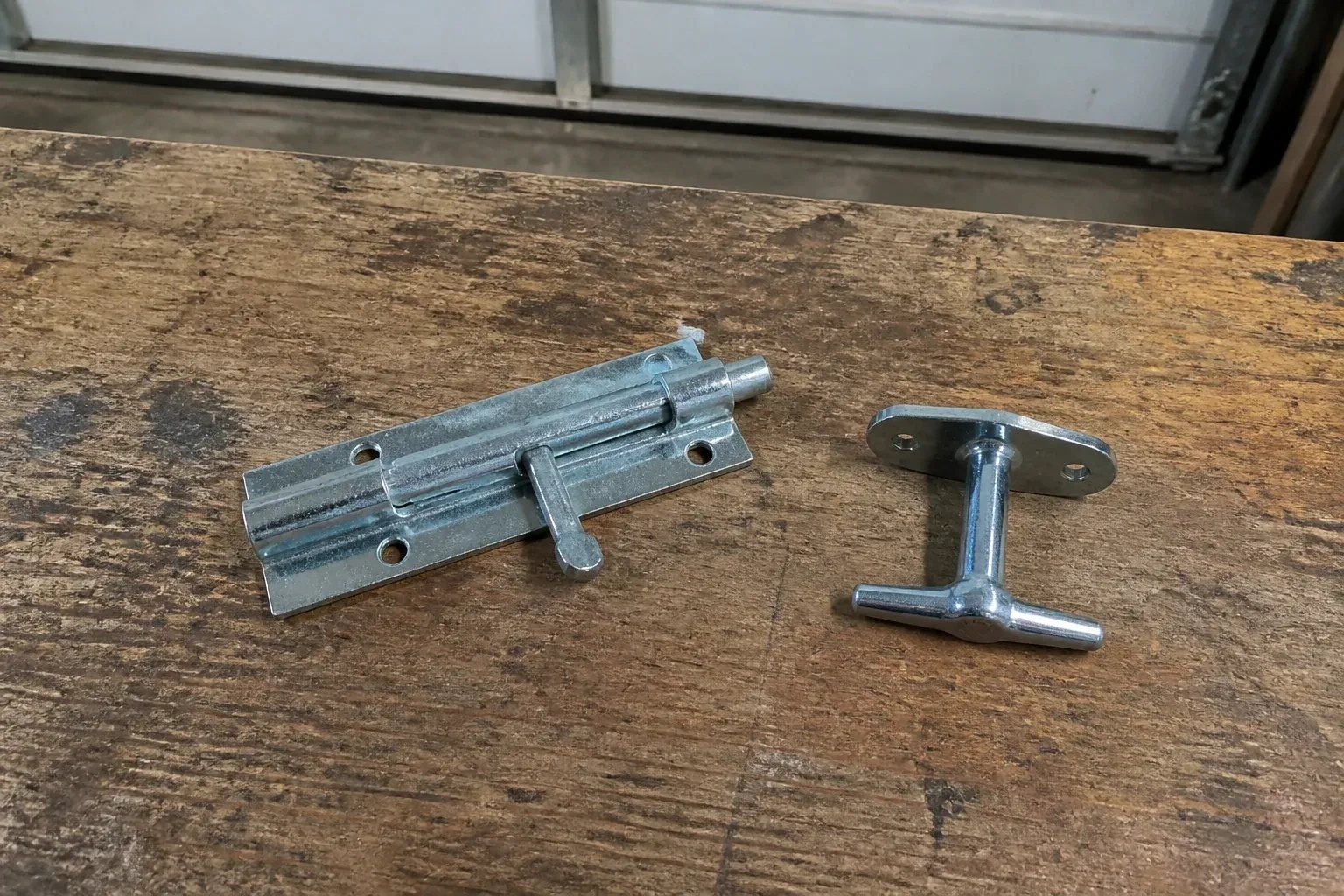 Detached slide bolt and T-handle on a wooden garage workbench. — Garage Door Manual Lock Repair, Brampton
