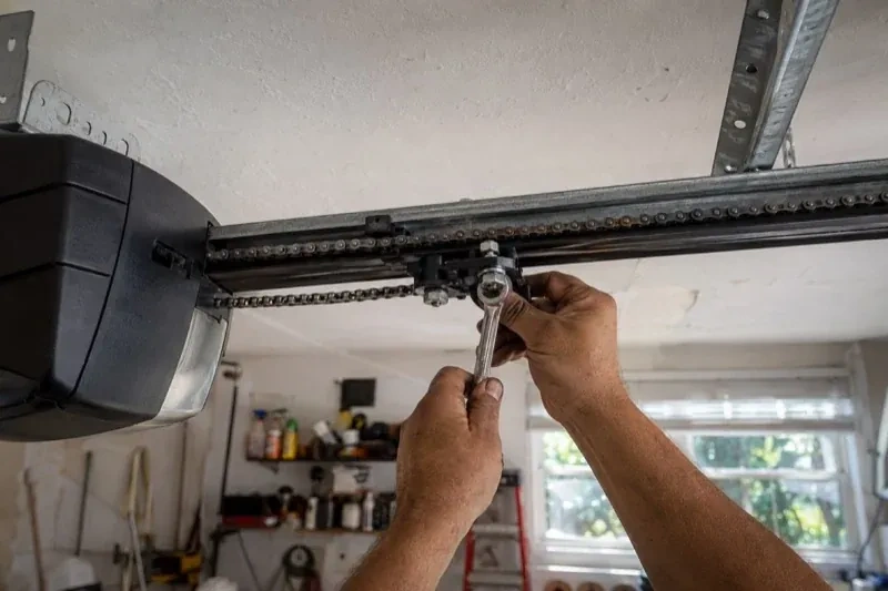 Hands holding a wrench against an opener trolley beneath a chain rail — Chain-Drive Opener Repair, Brampton