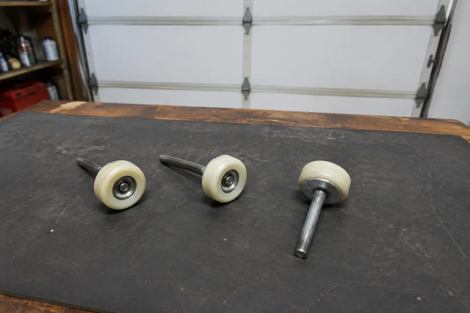 Three detached nylon-wheel garage door rollers with steel stems on a work mat. — Garage Door Roller Replacement, Brampton