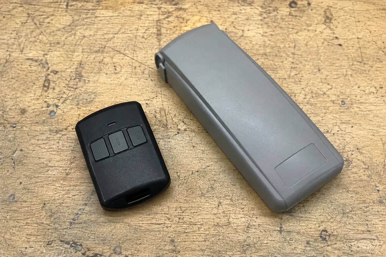 Three-button remote beside a closed grey keypad cover on a workbench. — Garage Door Remote and Keypad Programming, Brampton